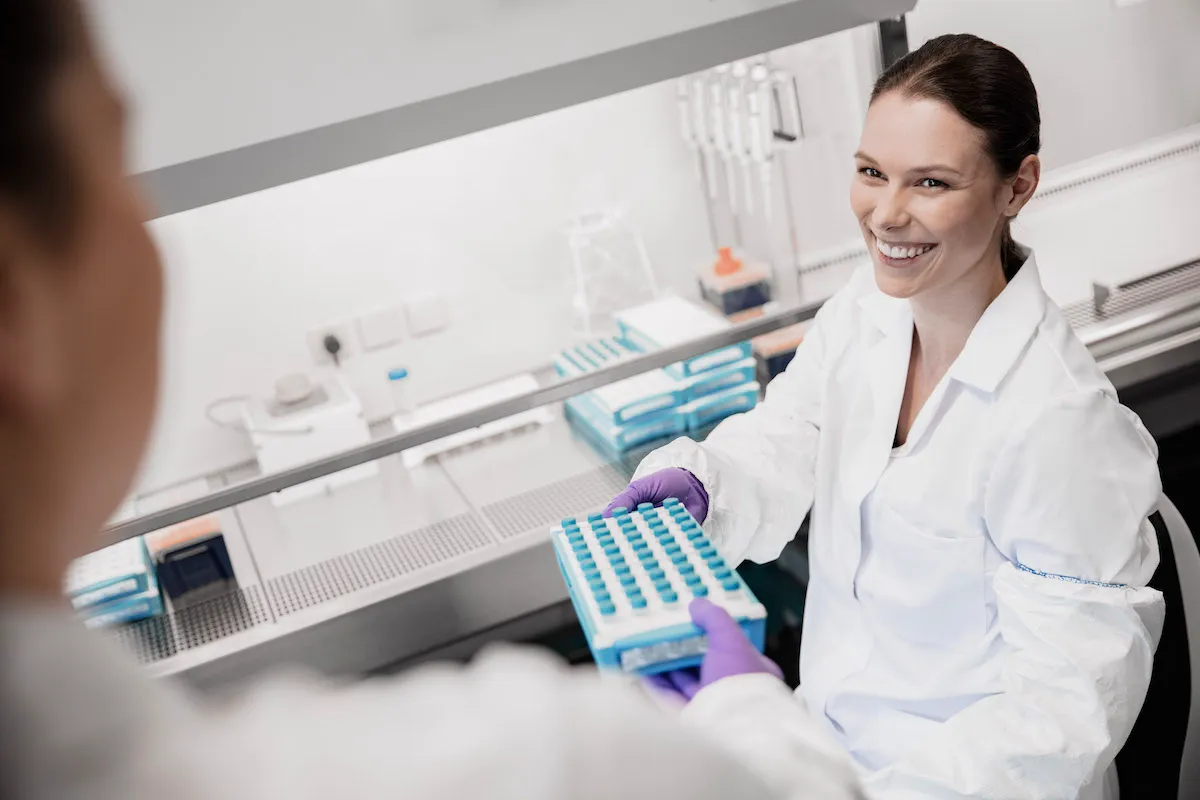 A seated female laboratory worker is seen from above, holding a tray of samples.